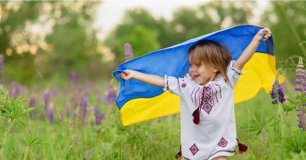 Маленька дитина біжить по полю з прапором