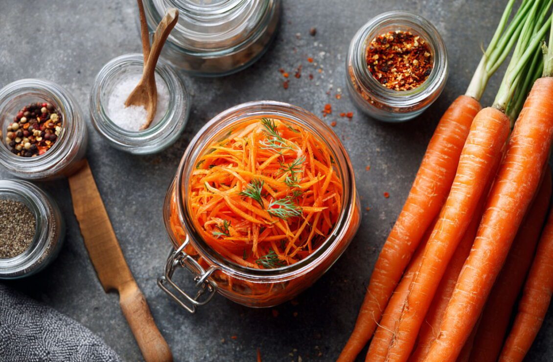 Салат моркви по-корейськи в банці, поруч цілі моркви та баночки зі спеціями
