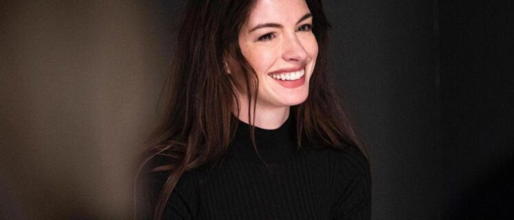 Усміхнена Енн Гетевей у чорному светрі на темному фоні