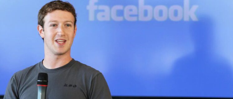 Марк Цукерберг в сірій футболці тримає мікрофон, виступаючи на заході у Facebook
